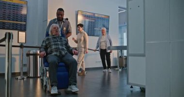 Güvenlik Kontrol Noktasındaki Kıdemli Gezgin: Tekerlekli sandalyeden kalkan yaşlı adam, Havaalanı Terminali 'ndeki X-ray Metal Detektör Tarayıcısını geçiyor, Havaalanı Personel Yardımcısı. Yolcu Ekran Prosedürleri.