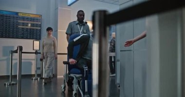 Havaalanı terminalindeki güvenlik kontrol noktası: Tekerlekli sandalyeden kalkan protez bacaklı adam, X-ray metal dedektörü tarayıcısını geçiyor, güvenlik personeli yardım ediyor. Tarama İşlemleri sırasında Yolcular.