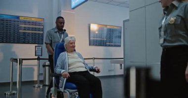 Havaalanı Terminali 'ndeki güvenlik kontrol noktası: Tekerlekli sandalyeden kalkan yaşlı kadın, metal detektör tarama kapısından geçen güvenlik görevlisi ona yardım ediyor. Tarama sırasında kıdemli turist.