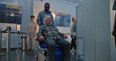 Havaalanı Terminali 'ndeki güvenlik kontrol noktası: Tekerlekli sandalyeden kalkan yaşlı adam, metal dedektör tarama kapısından geçen güvenlik görevlisi yardım ediyor. Tarama İşlemleri sırasında Yaşlı Turist.