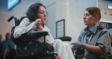 Güvenlik Kontrol Noktası: Havaalanı Terminali 'nde engelli bir kadını kontrol eden kadın havaalanı görevlisi. Uçağa binmek için yolcu tarama prosedürleri. Tekerlekli sandalyedeki gezgin seyahate çıkıyor. Ortam Kapalı.