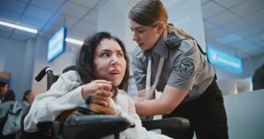 Güvenlik Kontrol Noktası: Havaalanı Terminalinde Fiziksel Engelli Kadın Yolcusunu Denetleyen TSA Memuru. Uçağa binmek için tarama prosedürleri. Tekerlekli sandalyedeki kadın seyahate çıkıyor. Orta Çekim.