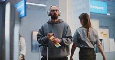 Kalabalık Havaalanı Terminali: Kulaklıklı Adam Atıştırmalık Yiyiyor, Transfer ya da Uçuş için Havalimanı Biniş Salonunda Bekliyor. Gezgin Tatile Çıkıyor. Çeşitli İnsanlar ve Havalimanı Personeli Yürüyüşü.