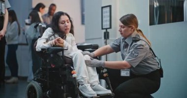 Havaalanı Terminali 'ndeki güvenlik kontrol noktası, kadın güvenlik görevlisi tekerlekli sandalyedeki kadını teftiş etti. TSA tarama prosedürleri. Yolcu ile Yürüyen İşçi Uçağa Biniş İçin Fiziksel Engelli.