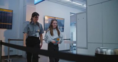 Havaalanı İşçisi, Kızla birlikte Havaalanı Terminalindeki Güvenlik Kontrol Noktasına Tarama Prosedürleri İçin Yürüyor. Bayan memur, genç kızı uçağa binmek için teftiş ediyor. Genç Turist Seyahate Çıkıyor. Yavaş Hareket.