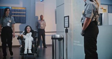 Güvenlik Kontrol Noktası: Havaalanı Terminali 'nde fiziksel engelli bir kadını kontrol eden kadın havaalanı görevlisi. Uçağa binmek için yolcu tarama prosedürleri. Tekerlekli sandalyedeki gezgin Seyahate çıkıyor.