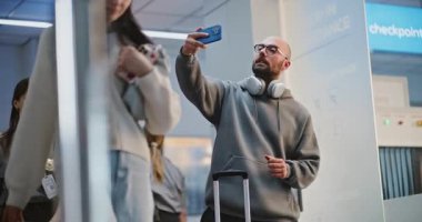 Kalabalık Havaalanı Terminali: Video Call ya da Recording Video Content tarafından telefonla konuşan bavullu turist. Gezgin Tatile Çıkıyor. Arka planda, Çeşitli İnsanlar ve Havaalanı Personeli Yürüyüşü.