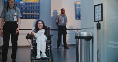 Güvenlik Kontrol Noktası: Havaalanı Terminali 'nde fiziksel engelli bir kadını kontrol eden kadın havaalanı görevlisi. Uçağa binmek için yolcu tarama prosedürleri. Tekerlekli sandalyedeki gezgin Seyahate çıkıyor.