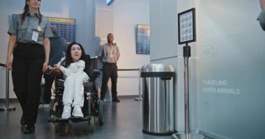 Güvenlik işçisi, fiziksel engelli bir kadınla birlikte havaalanı terminalindeki güvenlik kontrol noktasına yürüyor. Bayan memur tekerlekli sandalyedeki yolcuyu denetliyor. Uçağa binmek için Ulaşım Güvenliği İdaresi İnceleme Yöntemleri.