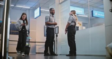 Kalabalık Uluslararası Havaalanı Terminali: Üniformalı İki Güvenlik Memuru Konuşuyor, Güvenlik Kontrol Noktasında Duruyor, Erkek Yolcuya Uçağı için Biniş Kapısı Gösteriliyor.