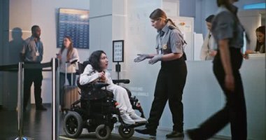 Havaalanı Terminali 'ndeki güvenlik kontrol noktası: Uçuş için tekerlekli sandalyedeki yolcuları denetleyen kadın güvenlik görevlisi. Tarama prosedürleri. Fiziksel Engelli Kadın Seyahate Çıkıyor. Tam Vuruş.