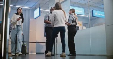 Kalabalık Uluslararası Havaalanı Terminali: Üniformalı İki Güvenlik Memuru Konuşuyor, Güvenlik Kontrol Noktasında Duruyor, Kadına Yardım Ediyor. Bagajı Uçuşlara Giden Çeşitli İnsanlar.