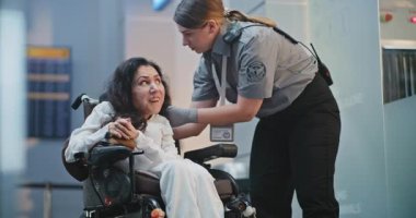 Güvenlik Kontrol Noktası: Havaalanı Terminali 'nde fiziksel engelli bir kadını kontrol eden kadın havaalanı görevlisi. Uçağa binmek için yolcu tarama prosedürleri. Tekerlekli sandalyedeki gezgin Seyahate çıkıyor.