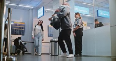 Havalimanı Terminali 'nde Duygusal Aile Buluşması: Mutlu Adam Ailesini Tatil Gezisinden Dönüşünü Kutluyor, Kızını Kollarıyla Kaldırıyor. Yatılı uçuşlar için çeşitli insanlar bavulla yürüyor. Yavaş Hareket.