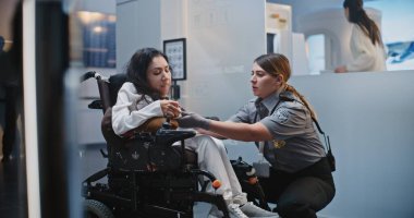 Güvenlik Kontrol Noktası: Havaalanı Terminali 'nde fiziksel engelli bir kadını kontrol eden kadın havaalanı görevlisi. Uçağa binmek için yolcu tarama prosedürleri. Tekerlekli sandalyedeki gezgin Seyahate çıkıyor.