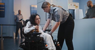 Güvenlik Kontrol Noktası: Havaalanı Terminali 'nde fiziksel engelli bir kadını kontrol eden kadın havaalanı görevlisi. Uçağa binmek için yolcu tarama prosedürleri. Tekerlekli sandalyedeki gezgin Seyahate çıkıyor.