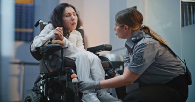 Güvenlik Kontrol Noktası: Havaalanı Terminali 'nde fiziksel engelli bir kadını kontrol eden kadın havaalanı görevlisi. Uçağa binmek için yolcu tarama prosedürleri. Tekerlekli sandalyedeki gezgin Seyahate çıkıyor.