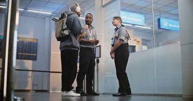 Kalabalık Uluslararası Havaalanı Terminali: Üniformalı İki Güvenlik Memuru Konuşuyor, Güvenlik Kontrol Noktasında Duruyor, Erkek Yolcuya Uçağı için Biniş Kapısı Gösteriliyor.