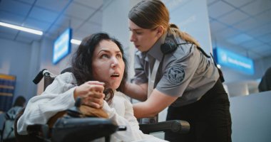 Güvenlik Kontrol Noktası: Havaalanı Terminalinde Fiziksel Engelli Kadın Yolcusunu Denetleyen TSA Memuru. Uçağa binmek için tarama prosedürleri. Tekerlekli sandalyedeki kadın seyahate çıkıyor. Orta Çekim.