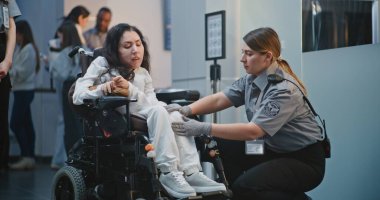 Havaalanı Terminali 'ndeki güvenlik kontrol noktası, kadın güvenlik görevlisi tekerlekli sandalyedeki kadını teftiş etti. TSA tarama prosedürleri. Yolcu ile Yürüyen İşçi Uçağa Biniş İçin Fiziksel Engelli.