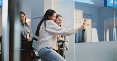 Kalabalık Havalimanı Terminali: Kızıyla Selfie Çeken Kadın, Uçak İndirme Merkezi 'nde Uçuşu Bekliyor. Aile Tatile Çıkıyor. Çeşitli İnsanlar ve Havalimanı Personeli Yürüyüşü.