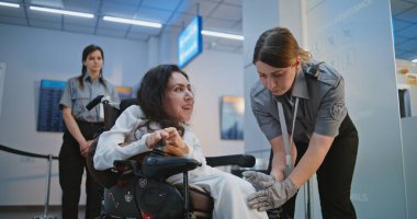 Güvenlik Kontrol Noktası 'ndaki tarama prosedürleri: Havaalanı Terminali' nde fiziksel engelli bir kadını kontrol eden kadın TSA memuru. Havalimanı İşçisi, Yolcuyla Yolcu Uçağı Uçuşu için Tekerlekli Sandalyede Yürüyor