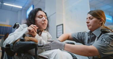 Güvenlik işçisi, fiziksel engelli bir kadınla birlikte havaalanı terminalindeki güvenlik kontrol noktasına yürüyor. Bayan memur tekerlekli sandalyedeki yolcuyu denetliyor. Uçağa binmek için Ulaşım Güvenliği İdaresi İnceleme Yöntemleri.