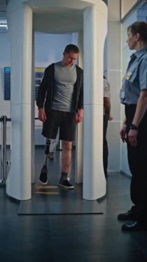 Havaalanı Terminalindeki güvenlik kontrol noktası: Protez bacaklı bir adam ve Metal dedektöründen geçen yetişkin bir kadın biniş için kapıları tarıyor. Tarama sırasında turistler. Dikey Çekim.