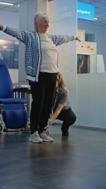 Güvenlik Kontrol Noktası: Havalimanı Terminali 'nde yaşlı kadını kontrol eden kadın, tekerlekli sandalyeye binen kadın. Uçuş için yolcu tarama prosedürleri. Engelli kıdemli gezgin. Dikey Çekim.