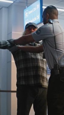 Güvenlik Kontrol Noktası: Afrikalı Amerikalı Ulaşım Güvenliği Memuru Havaalanında Yaşlı Adamı Kontrol Ediyor. Yolcu İndirme Prosedürleri ve Uçuş için Güvenlik Kontrolü. Son sınıf yolcusu seyahate çıkıyor. Dikey Çekim.