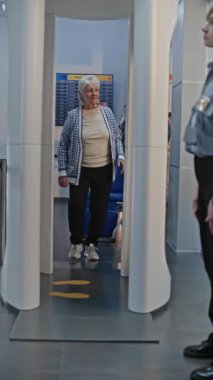 Güvenlik Kontrol Noktasındaki Kıdemli Gezgin: Tekerlekli sandalyeden kalkan yaşlı kadın, Havaalanı Personel Yardım Hatunu X-ray Metal Detektör Tarayıcısını geçiyor. Tarama prosedürleri. Dikey Çekim.