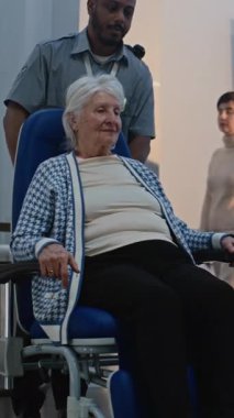 Havaalanındaki güvenlik kontrol noktası: Tekerlekli sandalyeden kalkan yaşlı kadın, Metal dedektöründen geçerek giriş kapılarını tarıyor. Tarama sırasında kıdemli turist. Dikey Çekim.