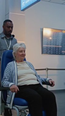 Havaalanındaki güvenlik kontrol noktası: Tekerlekli sandalyeden kalkan yaşlı kadın, metal detektör tarama kapısından geçen güvenlik görevlisi ona yardım ediyor. Gösterim sırasında kıdemli turist. Dikey Çekim.