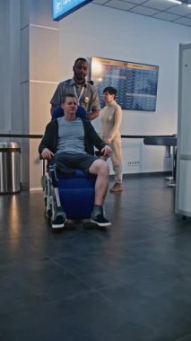 Havaalanındaki güvenlik kontrol noktası: Tekerlekli sandalyeden kalkan protez bacaklı adam, X-ray metal dedektörü tarayıcısını geçiyor, güvenlik personeli yardım ediyor. Gösterim sırasında yolcular. Dikey Çekim.