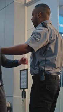 Havaalanı Terminalindeki güvenlik kontrol noktası: Afrikalı Amerikan Güvenlik Subayı Biyonik Protez Bacaklı Genç Adamı Uçuş için Denetliyor. TSA tarama prosedürleri. Engelli turist. Dikey Çekim.