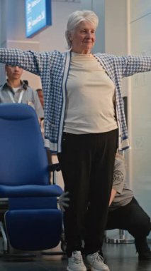 Havaalanı Terminali 'ndeki güvenlik kontrol noktası: Tekerlekli sandalyedeki yaşlı kadın ve yaşlı adamı denetleyen çeşitli güvenlik görevlileri. TSA tarama prosedürleri. Seyahate çıkan kıdemli turistler. Dikey Çekim.