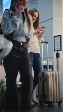 Kalabalık Havalimanı Terminali: Yetişkin Kadın Smartphone 'da Selfie Çekiyor, Uçağa Biniş Salonu' nda Bekliyor. Seyahate çıkan bir turist. Çeşitli İnsanlar ve Havalimanı Personeli Yürüyüşü. Dikey Çekim.