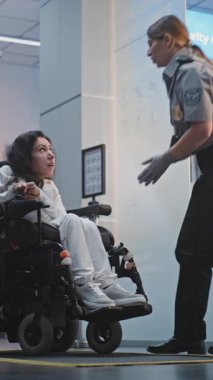 Havaalanı Terminali 'ndeki güvenlik kontrol noktası, kadın güvenlik görevlisi tekerlekli sandalyedeki kadını teftiş etti. TSA tarama prosedürleri. Yolcu ile Yürüyen İşçi Engelli Uçuşu. Dikey Çekim.