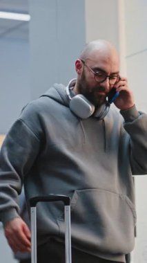 Kalabalık Uluslararası Havaalanı Terminali: Cep telefonuyla konuşan, elini sallayan, uçağa binmeyi bekleyen bavullu adam. Arka planda, Çeşitli İnsanlar ve Havalimanı Personel Yürüyüşü. Dikey Çekim.