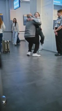 Uluslararası Havaalanı Terminali 'nde ailesiyle buluşan mutlu adam kızını kucağına alır. Duygusal Aile Birleşmesi. Çeşitli insanlar, bavulla yürüyen yolcular. Dikey Çekim.