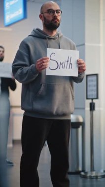 Uluslararası Havalimanı Terminali: Havalimanı karşılama kartı, uçak yolcularını karşılama. Çeşitli İnsanlar Bavulla Yürüyor. İş ya da Ulaştırma Servisi. Dikey Çekim