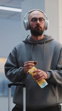 Kalabalık Havaalanı Terminali: Kulaklıklı Adam Atıştırmalık Yiyor, Uçağa Biniş Salonu 'nda Uçuş Bekliyor. Gezgin Tatile Çıkıyor. Çeşitli insanlar, havaalanı personeli yürüyüşü. Dikey Çekim.