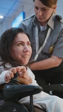 Güvenlik Kontrol Noktası 'ndaki tarama prosedürleri: Havaalanında fiziksel engelli bir kadını kontrol eden kadın havaalanı görevlisi. Havaalanı İşçisi, Yolcuyla Yolcu Biniş Uçuşu için Tekerlekli Sandalyede Geziniyor. Dikey Çekim