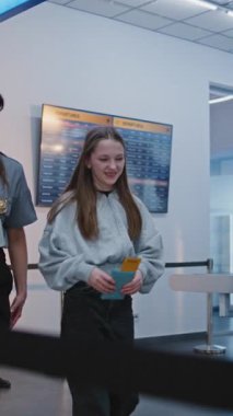 Havaalanı İşçisi, Kızla birlikte Havaalanı Terminalindeki Güvenlik Kontrol Noktasına Tarama Prosedürleri İçin Yürüyor. Bayan memur, genç kızı teftiş ediyor. Genç Turist Seyahate Çıkıyor. Ağır çekim. Dikey Çekim.