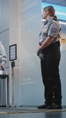 Kalabalık Uluslararası Havaalanı Terminali: Güvenlik Kontrol Noktasında Duran Güvenlik Personeli, Biniş Uçuşlarına Giden Çeşitli İnsanlar, Varış ve Gidiş Kurulunu Denetleme. Dikey Çekim.