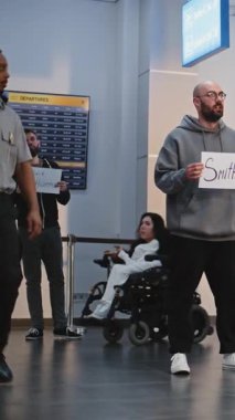 Uluslararası Havalimanı Terminali 'nde Ulaştırma Servisi: Havalimanı karşılama görevlileri isim işareti tutuyor, Uçak Yolcularını Bekliyor. Çeşitli İnsanlar ve Gezginler Yürüyor. Tam doz. Dikey Çekim.