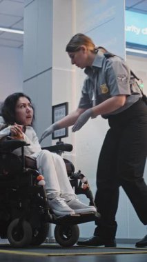 Güvenlik Kontrol Noktası: Havaalanı Terminali 'nde fiziksel engelli bir kadını kontrol eden kadın havaalanı görevlisi. Uçağa binmek için tarama prosedürleri. Tekerlekli sandalyedeki gezgin seyahate çıkıyor. Dikey Çekim