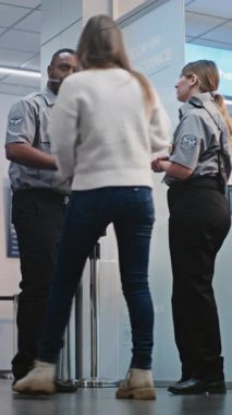 Kalabalık Uluslararası Havaalanı Terminali: İki farklı güvenlik görevlisi konuşuyor, Güvenlik Kontrol Noktasında duruyor, Kadına Yardım Ediyor. Bagajı Uçuşlara Giden Çeşitli İnsanlar. Dikey Çekim.