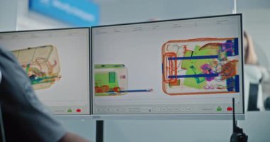 Havaalanı Güvenlik Kontrol Noktası: Güvenlik Subayı Bilgisayar Ekranları Yazılım Kullanarak Bavul X-ray taramasını kontrol ediyor. Arka planda, Tarama İşlemleri sırasında El Bagajı Olan Çeşitli İnsanlar.