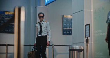 Havaalanı Terminalindeki Uçuş Ekibi: Havaalanı Kaptanı, İki Güzel Hostes Ticari Uçuş için Bavullarla Yürüyor, Güvenlik Kontrol Noktasında Bayan TSA memurunun yanından geçiyor. Yavaş Hareket